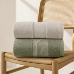 Serenity Textured Towels in beige and sage green stacked on a rattan chair